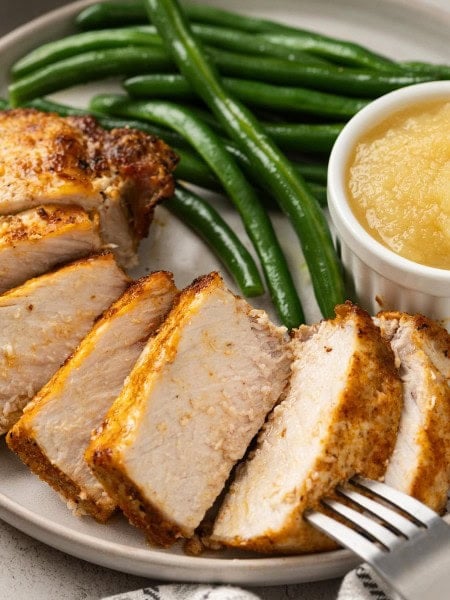 Juicy Air Fryer Pork Chops sliced on a plate with green beans and applesauce.