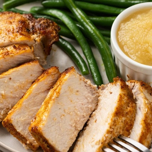 Juicy Air Fryer Pork Chops sliced on a plate with green beans and applesauce.