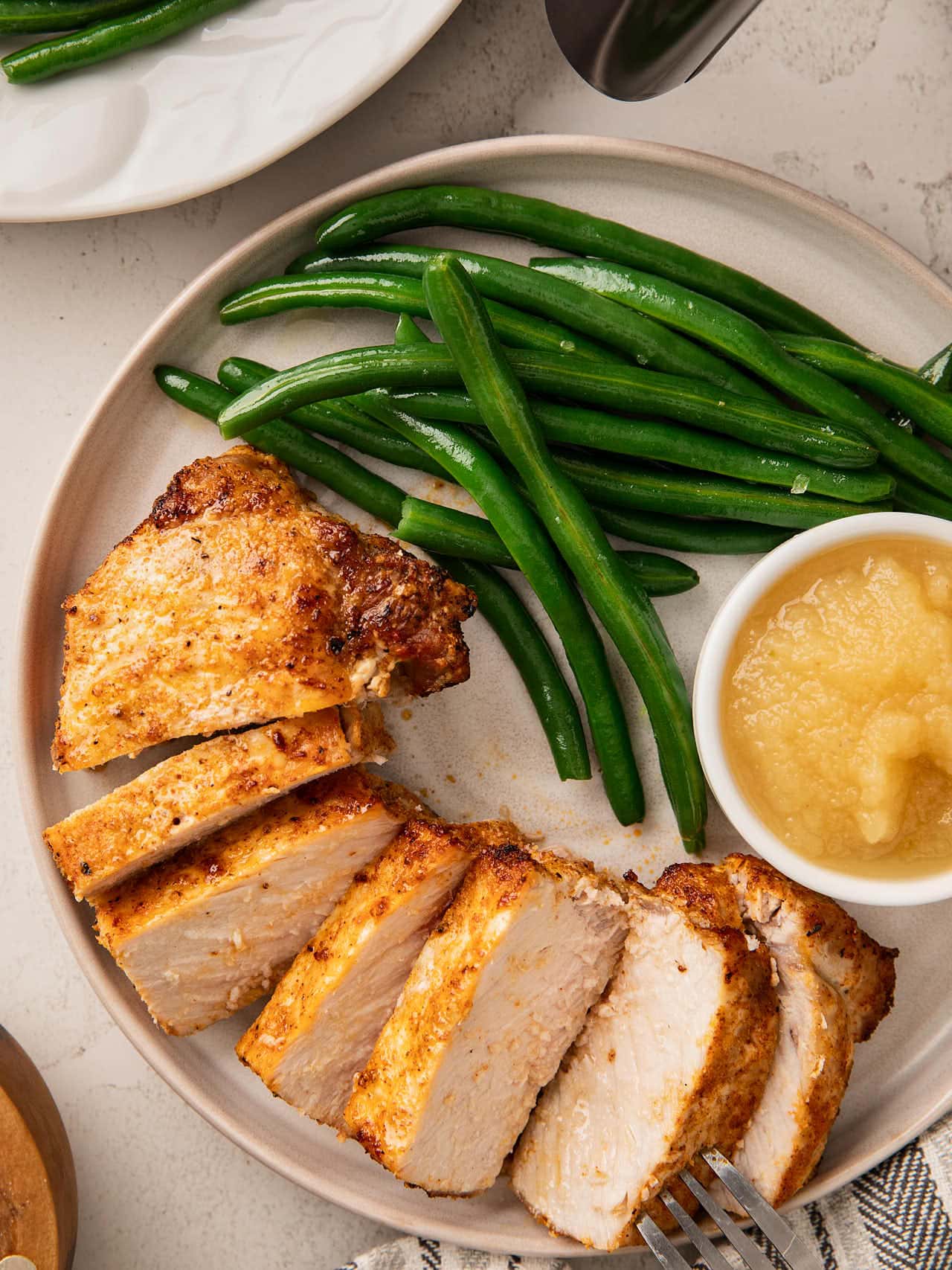 Overhead view of sliced Air Fryer Pork Chops fanned on a plate with green beans and applesauce.