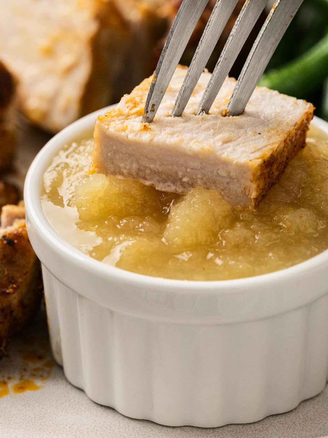 A fork holding a bite of Air Fryer Pork Chops over a bowl of applesauce