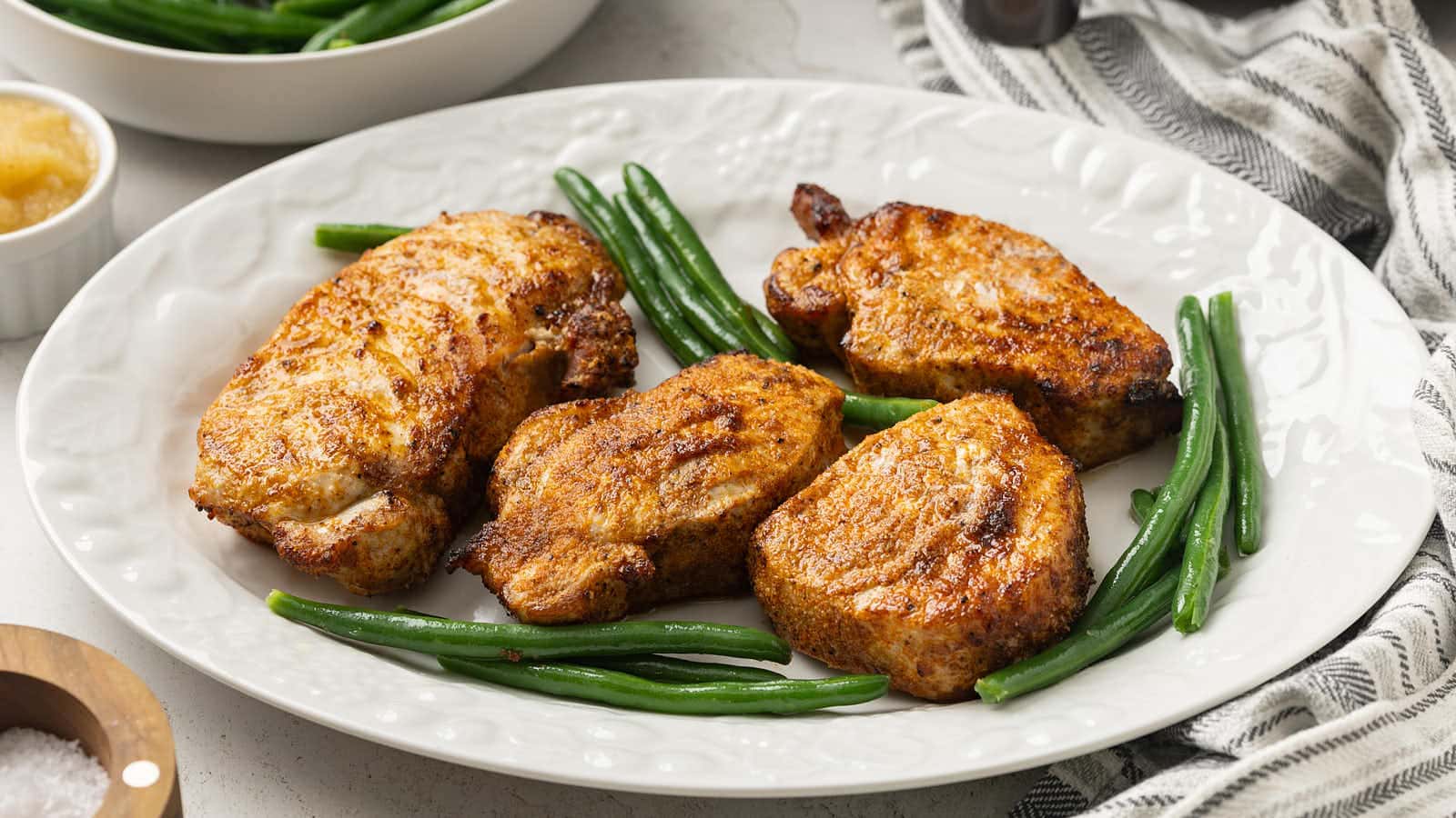 Air Fryer Pork Chops on a white platter with green beans.