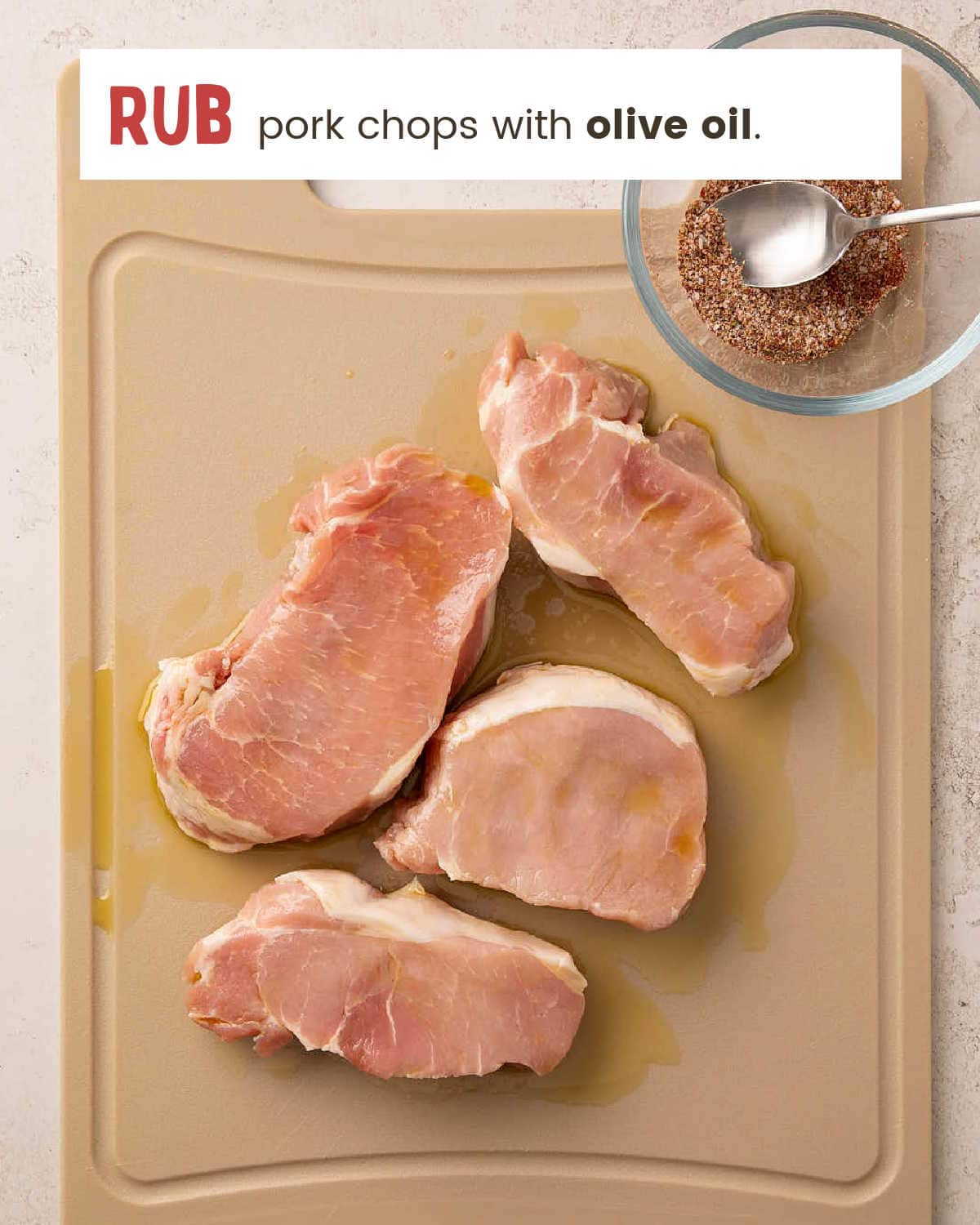 Four raw pork chops rubbed with olive oil on a cutting board .