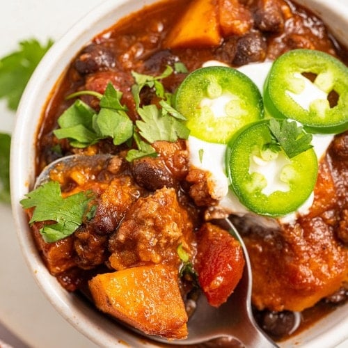Close-up of Crockpot Ground Turkey Chili with sour cream, jalapeño slices and a sweet potato cube on a spoon.