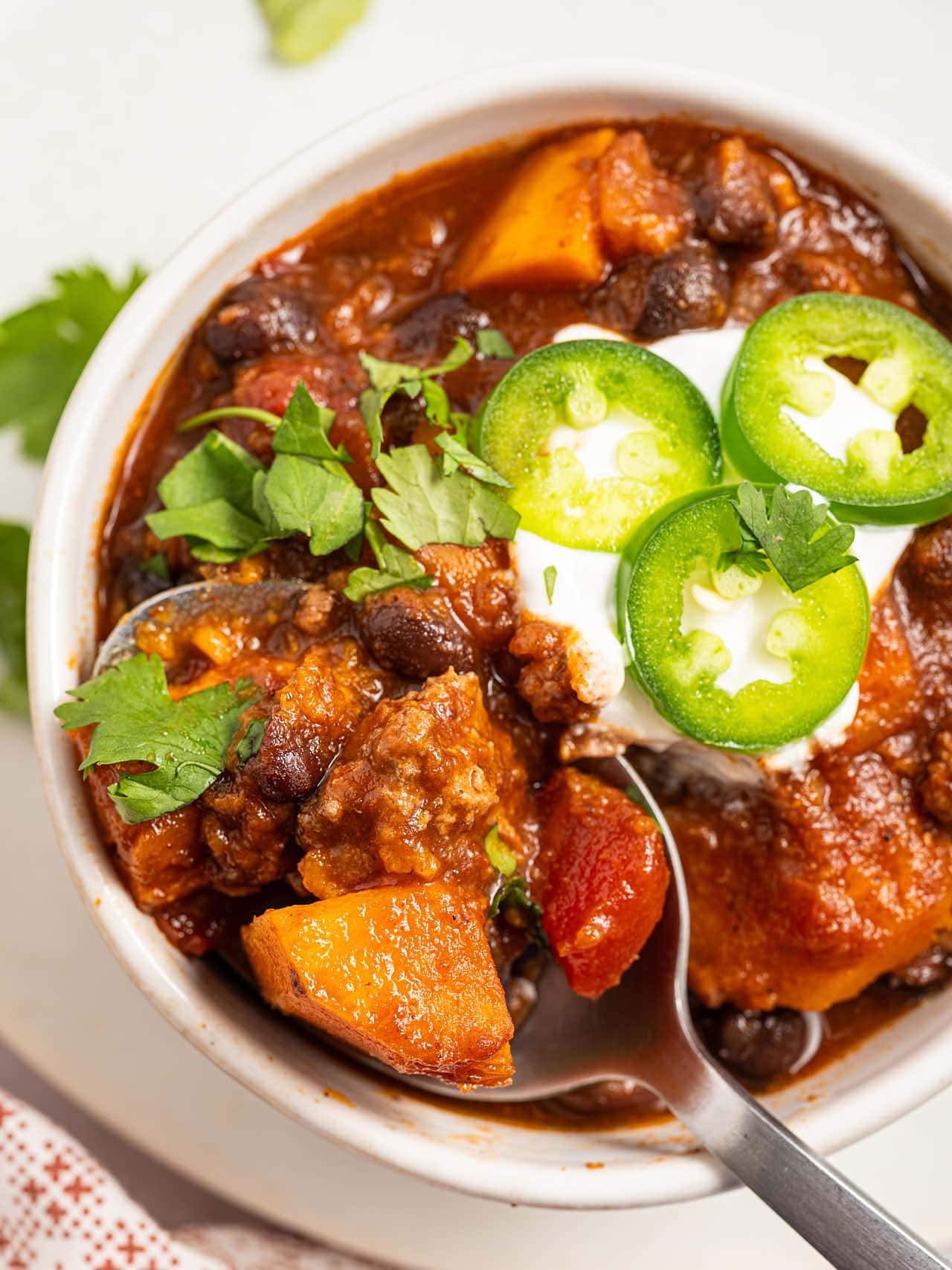 Close-up of Crockpot Ground Turkey Chili with sour cream, jalapeño slices and a sweet potato cube on a spoon.