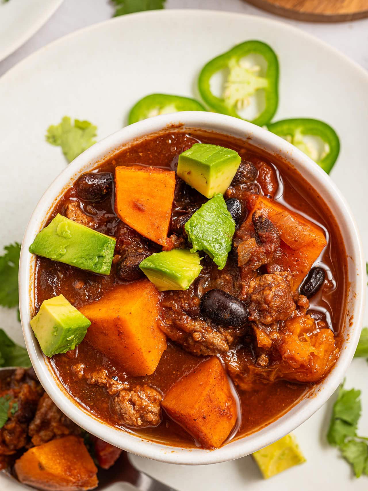 Overhead bowl of Crockpot Ground Turkey Chili topped with diced avocado, jalapeño slices on the plate.
