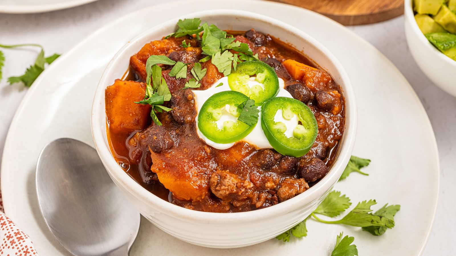Bowl of Crockpot Ground Turkey Chili topped with sour cream, jalapeño slices and cilantro, spoon on the plate.