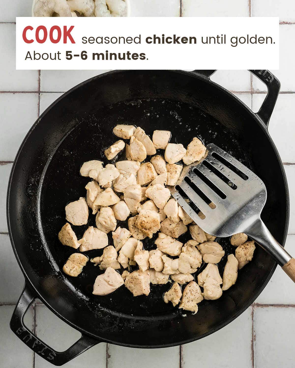 Diced chicken cooking in a cast iron skillet.