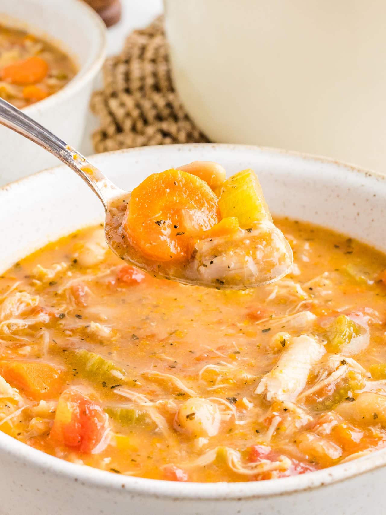 Close-up of a spoonful of carrot, celery and shredded chicken held over a bowl of soup.