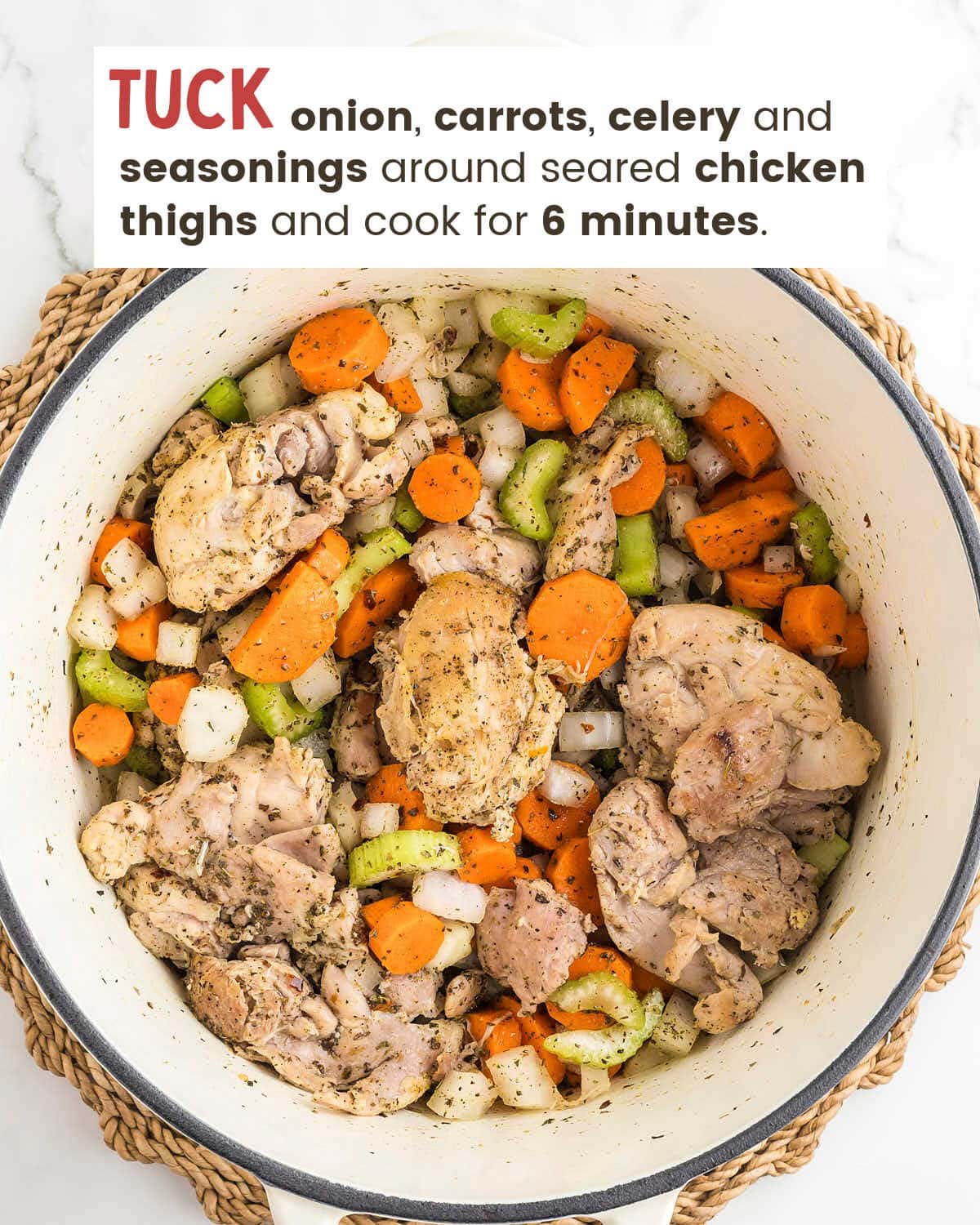 Seared chicken thighs in a white Dutch oven with sliced carrots, diced onion and celery.
