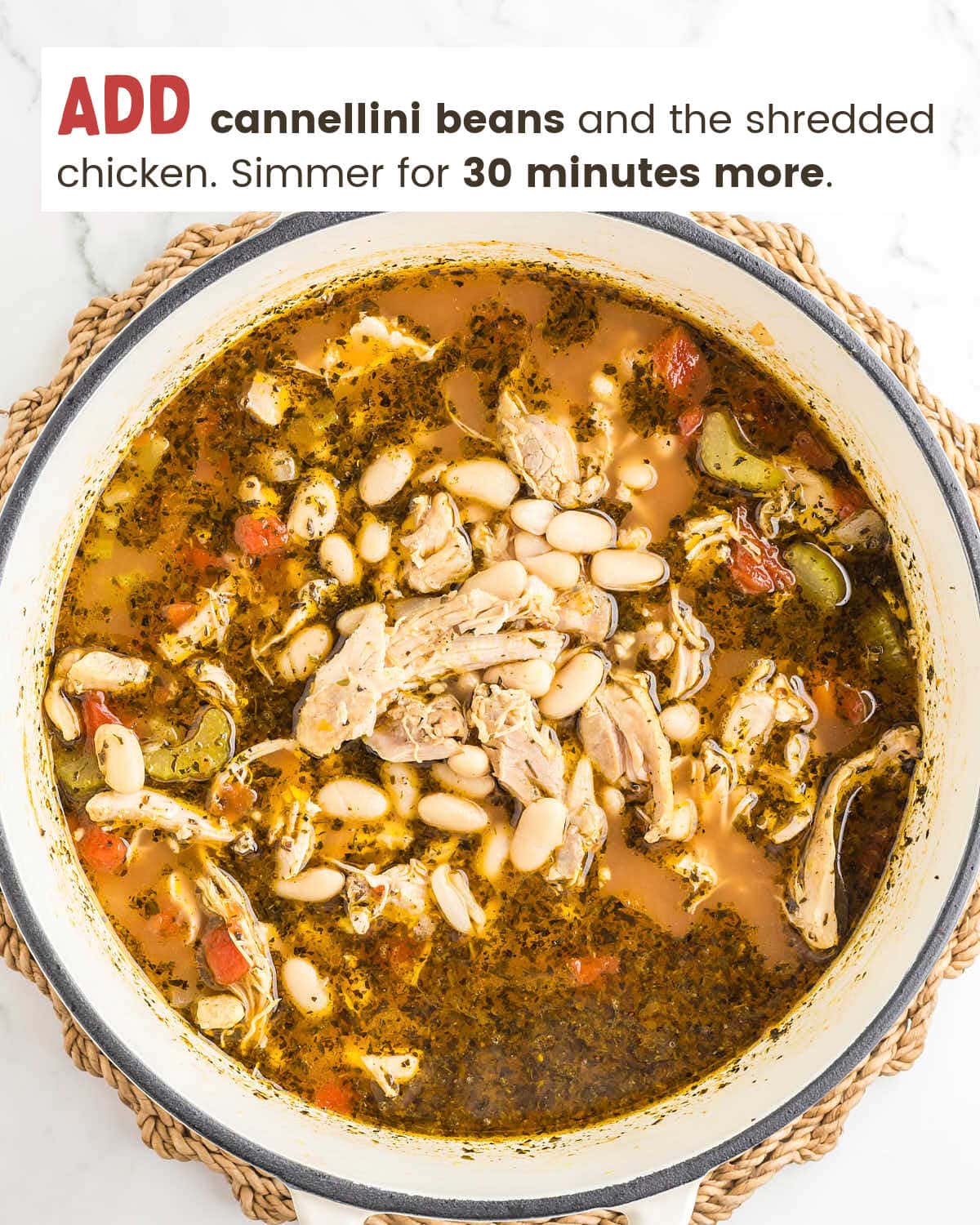 Shredded chicken and cannellini beans stirred into the broth in a white Dutch oven.