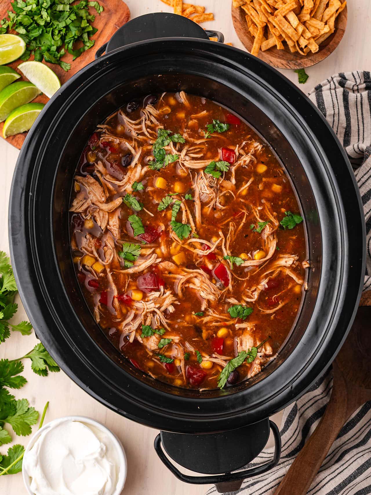 Overhead view of Crockpot Chicken Enchilada Soup in a black slow cooker with a wooden ladle and fresh cilantro.