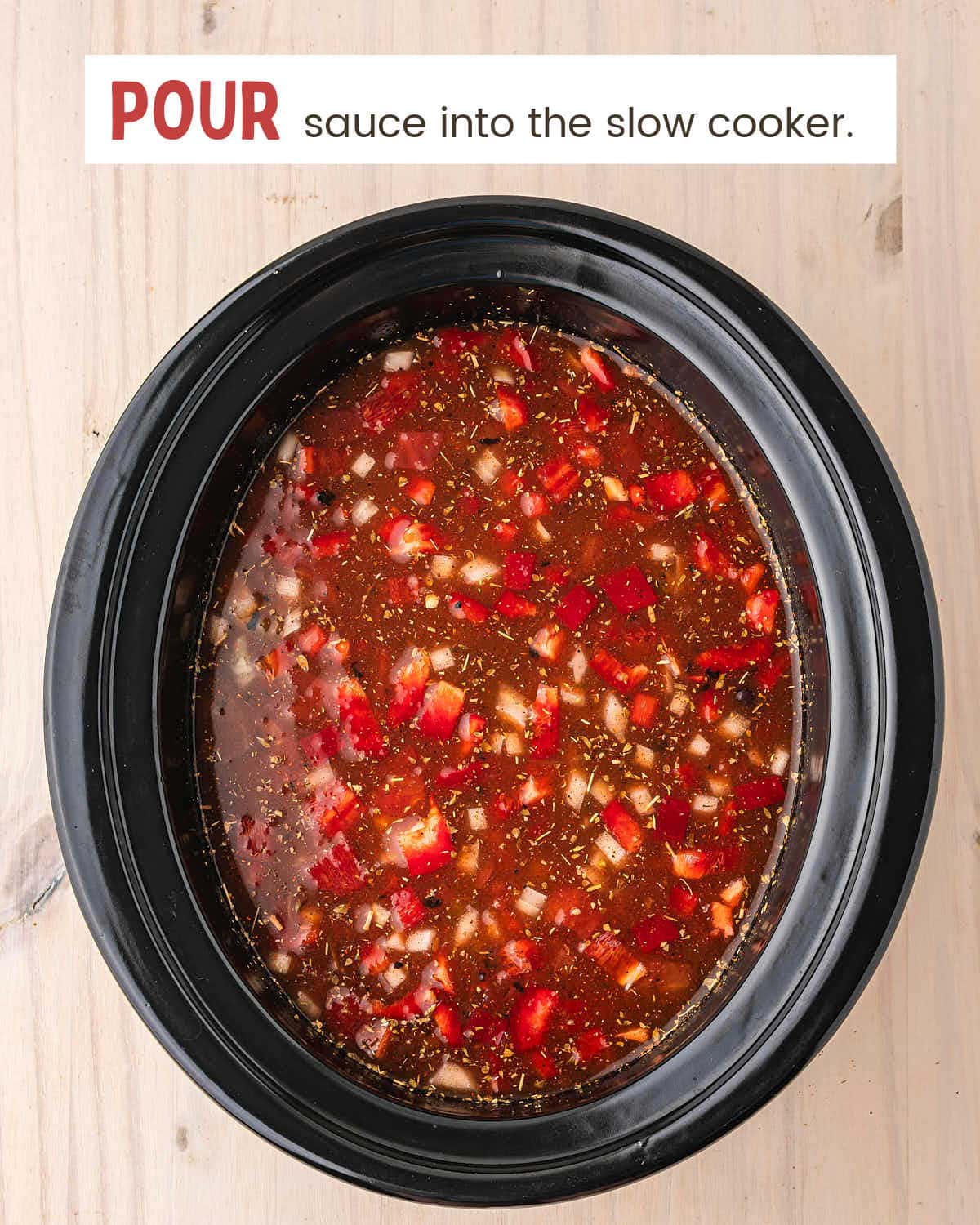 Enchilada sauce broth poured over the vegetables and chicken in a black slow cooker before cooking.