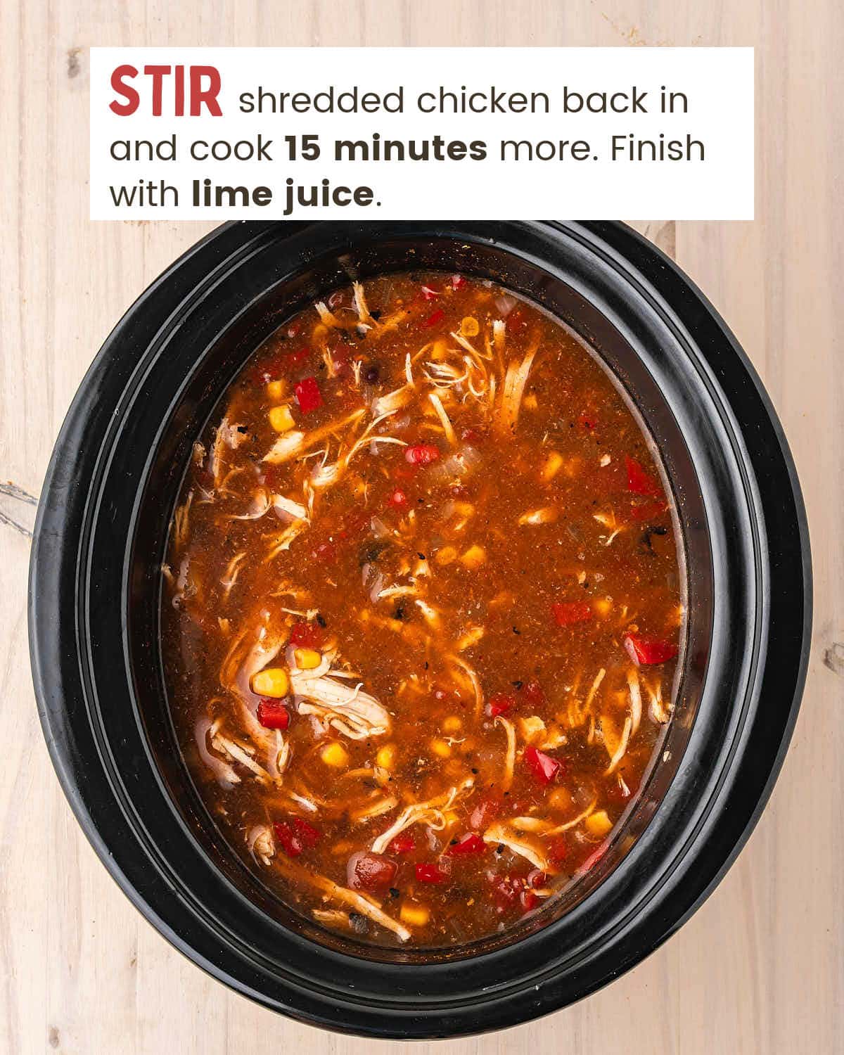 Shredded chicken stirred back into the enchilada soup in a black slow cooker.