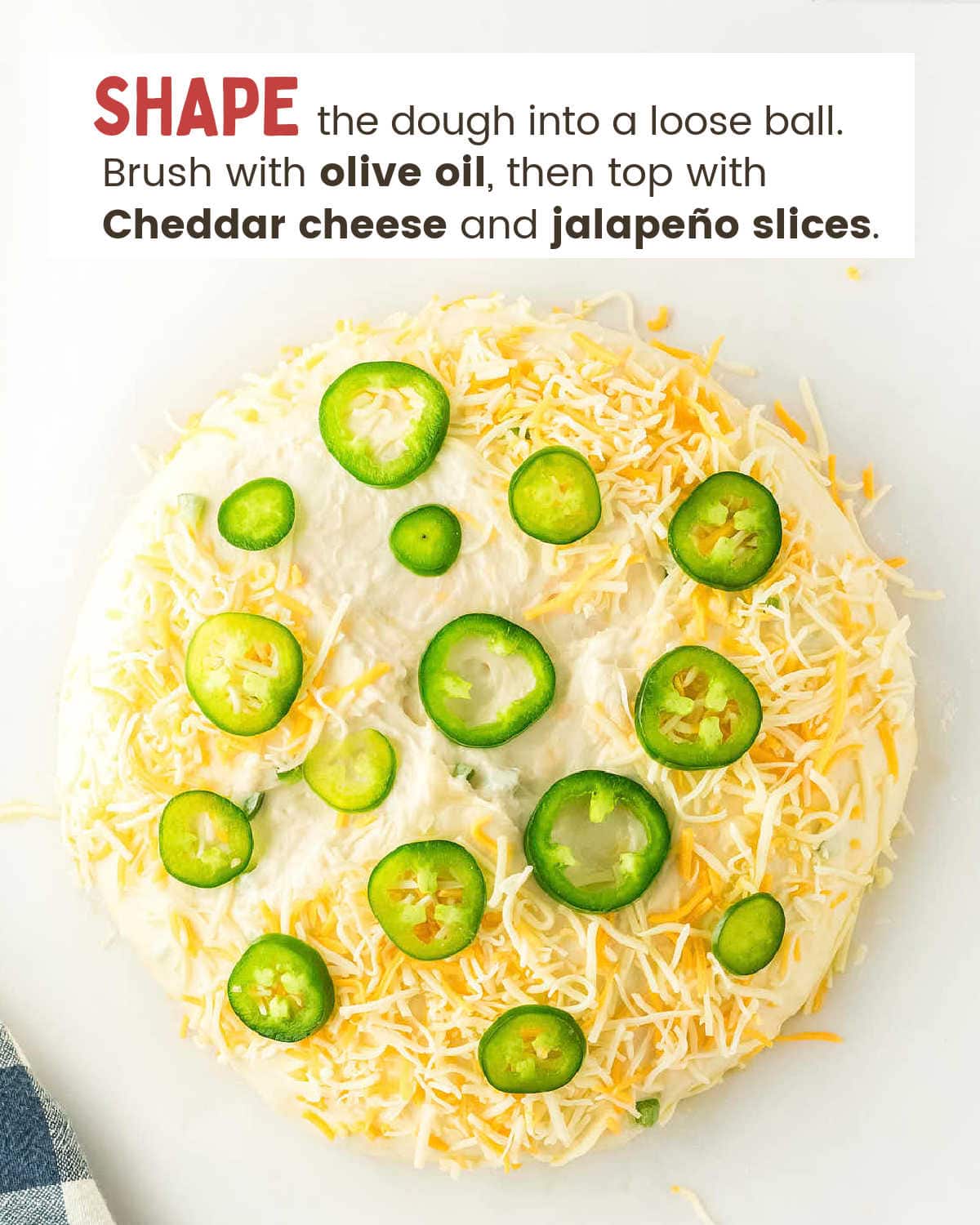 Shaped dough topped with shredded cheese and fresh jalapeño slices before baking.