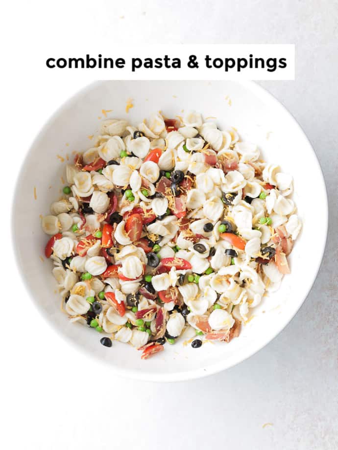 Combine pasta, peas, tomatoes, olives, bacon, and cheddar cheese in a large salad bowl