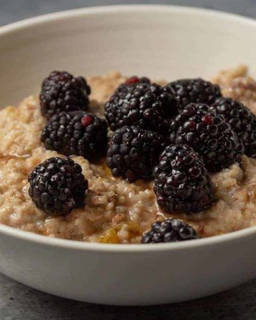 A bowl of berry oatmeal with blackberries, crushed pecans, and maple syrup.