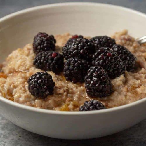 A bowl of berry oatmeal with blackberries, crushed pecans, and maple syrup.