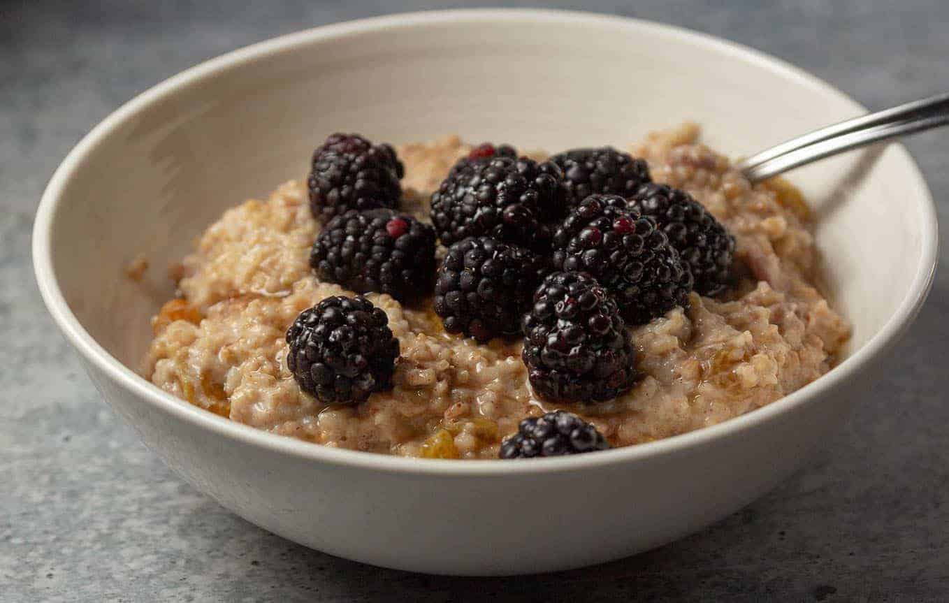 A bowl of berry oatmeal with blackberries, crushed pecans, and maple syrup.