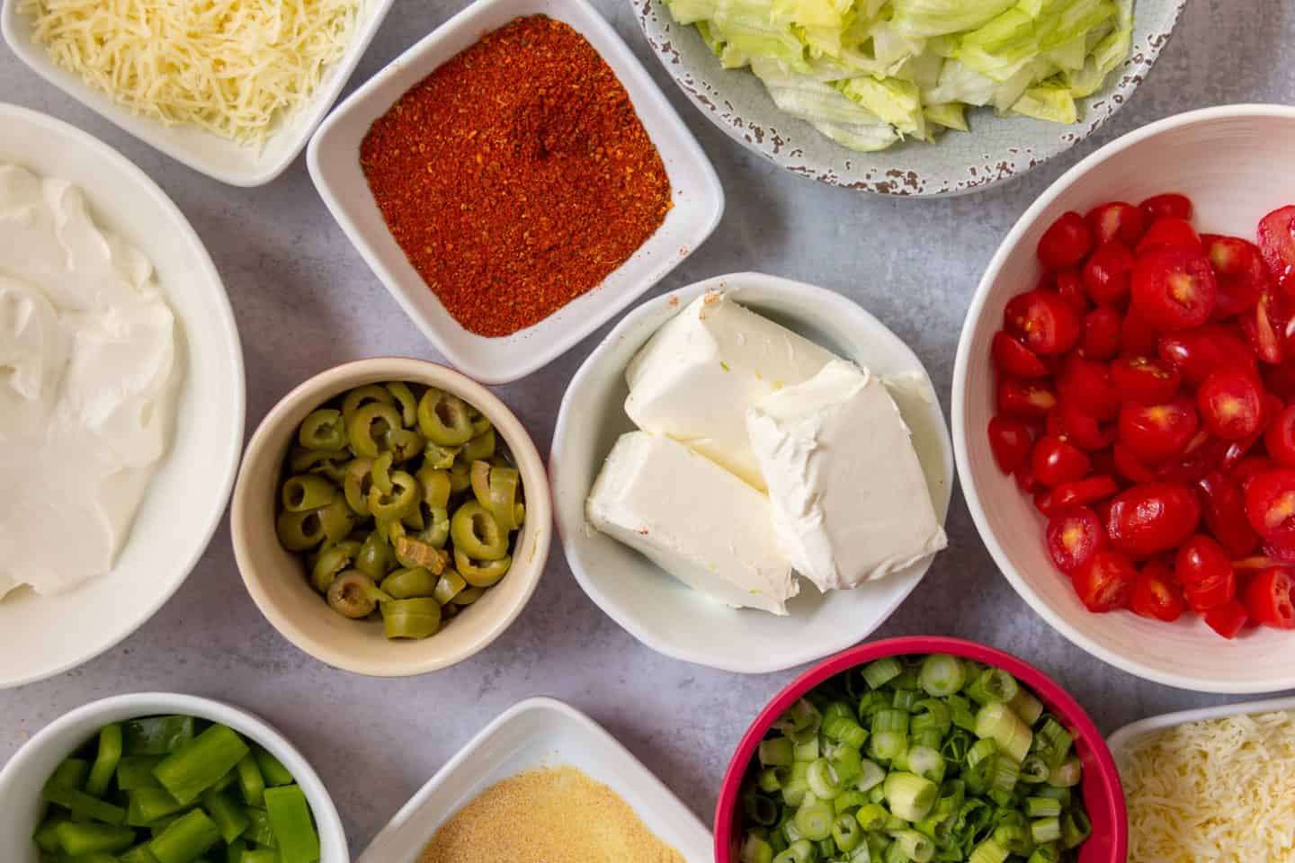 Topping options for Taco Dip: Cheddar cheese, Jack cheese, cherry tomatoes, iceberg lettuce, green onions, green peppers, olives